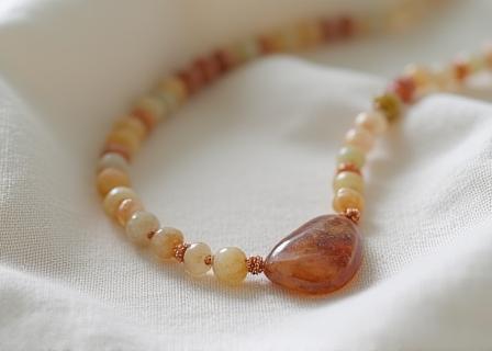 Delicate handmade beaded necklace with a natural stone pendant, resting on a fabric background.
